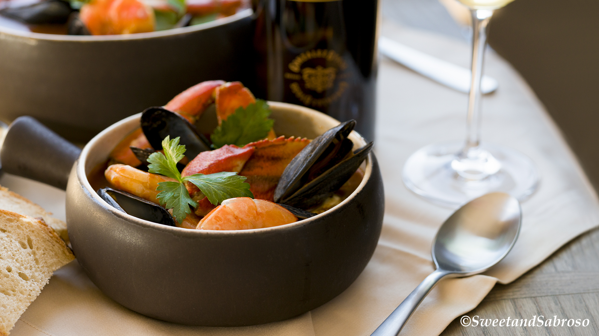 California-Coastal-Seafood-Stew-In-A-Bowl-With-Shrimp-Mussels-Dungeness-Crab-Garnished-with-Parsley-With-Serving-Bowl-And-Wine-In-Background