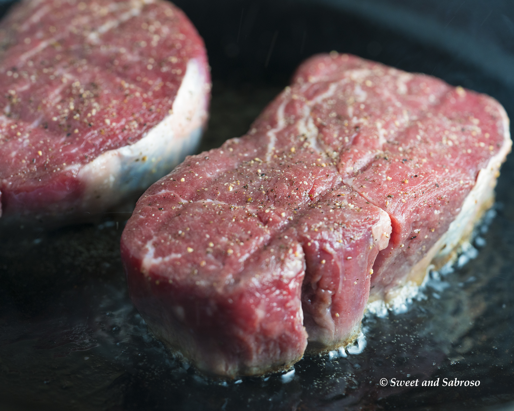 Perfect Pan Seared Restaurant Style Filet Mignon for Two - a close-up of raw steaks searing in a cast iron skillet 