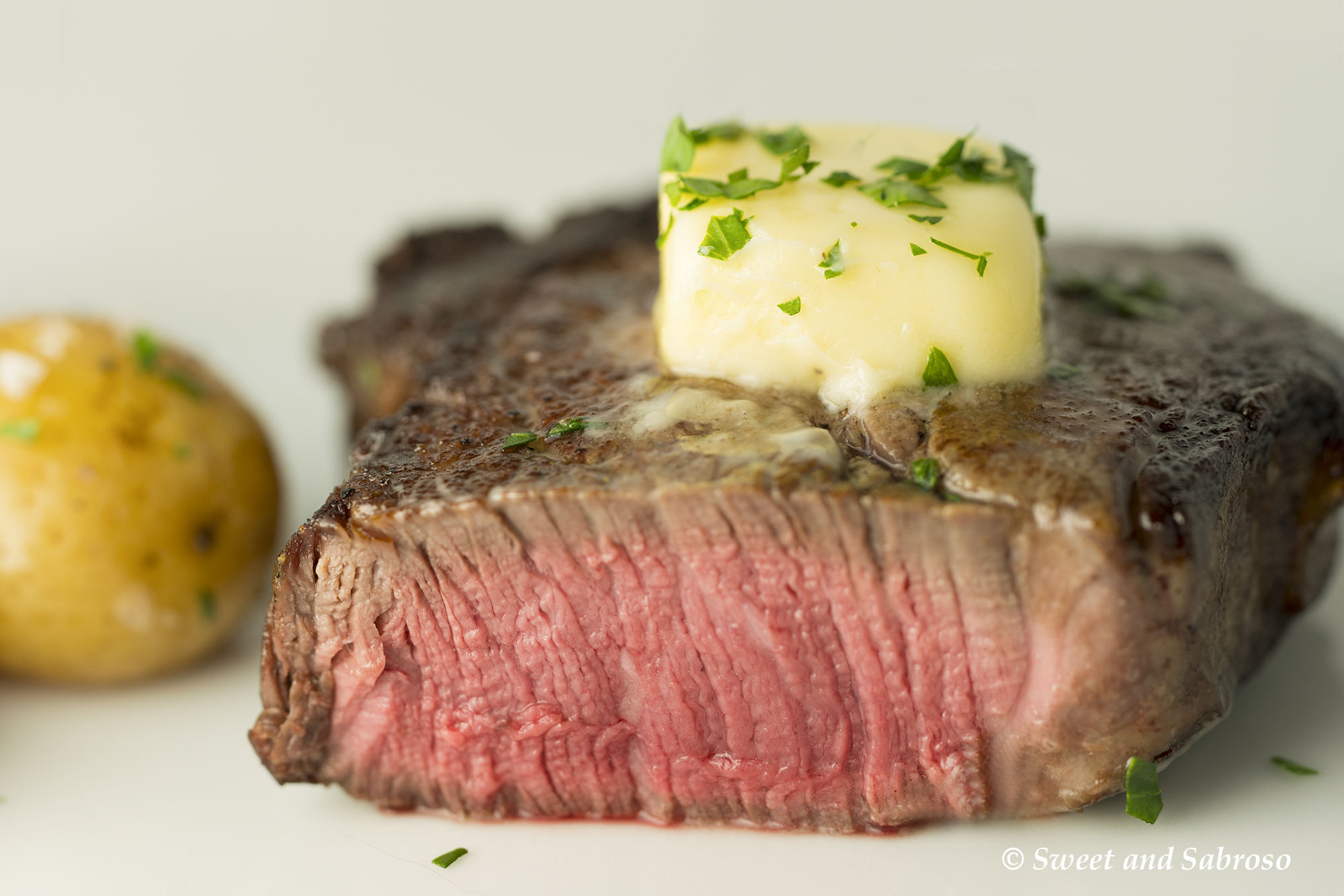Perfect Pan Seared Restaurant Style Filet Mignon pictured medium-rare with butter and parsley on top