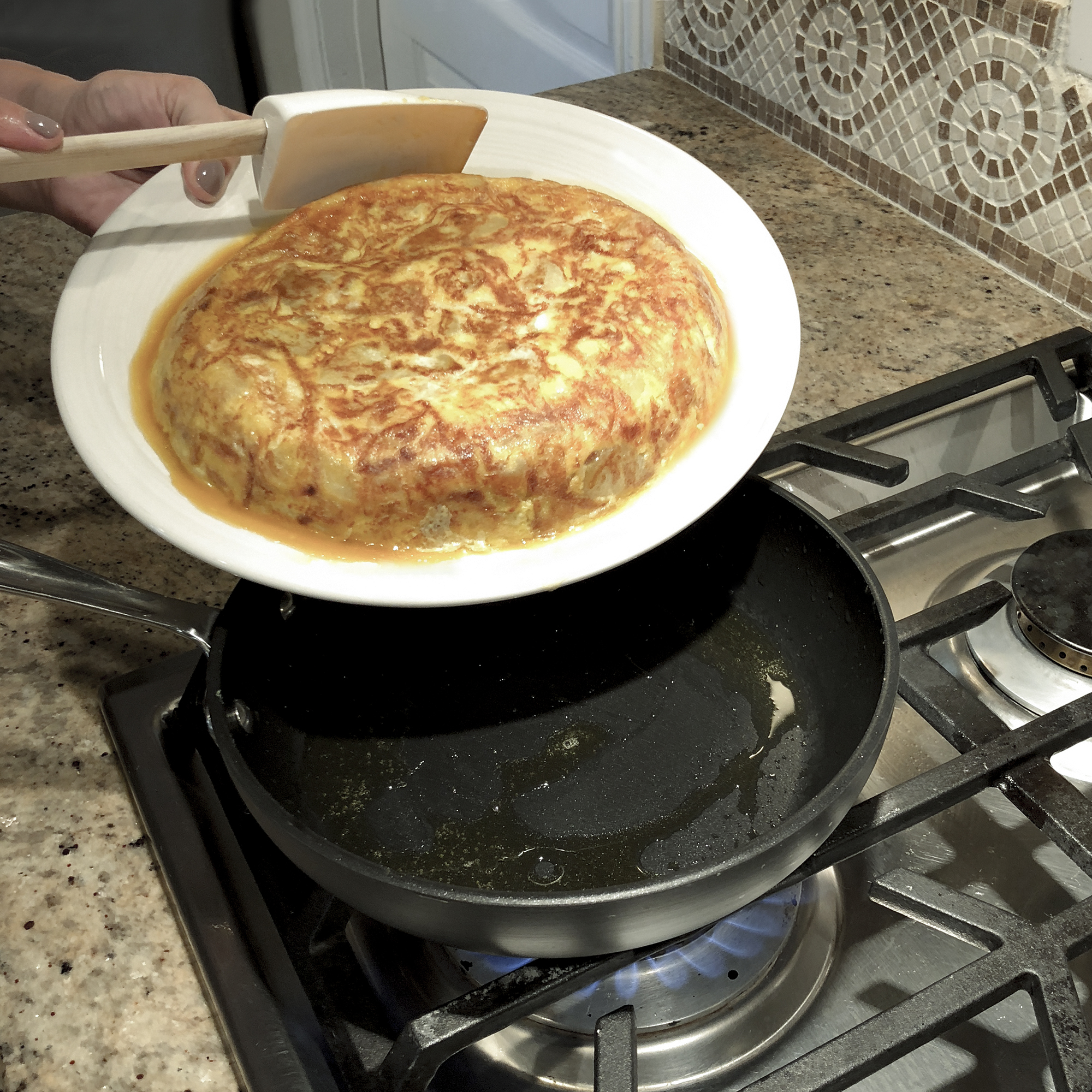 Tortilla Española (Spanish Omelet) that has been flipped onto a plate is being added back into pan to finish cooking